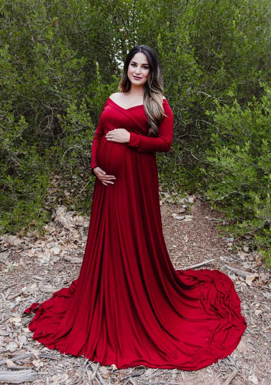 Smiling pregnant woman in front of green bushes in red dress