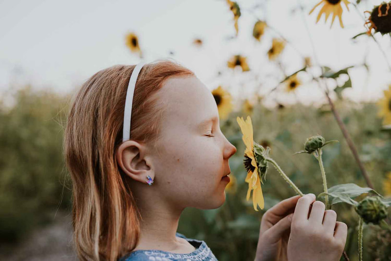 Young girl smells sunflower with eyes closed.